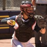 a softball catcher with a softball in her right hand and a softball mitt on her left hand