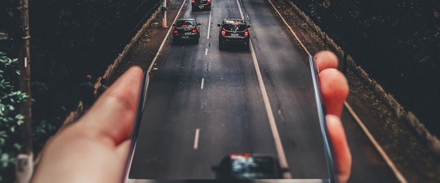 person holding a phone and the phone transitioning in to a road with cars